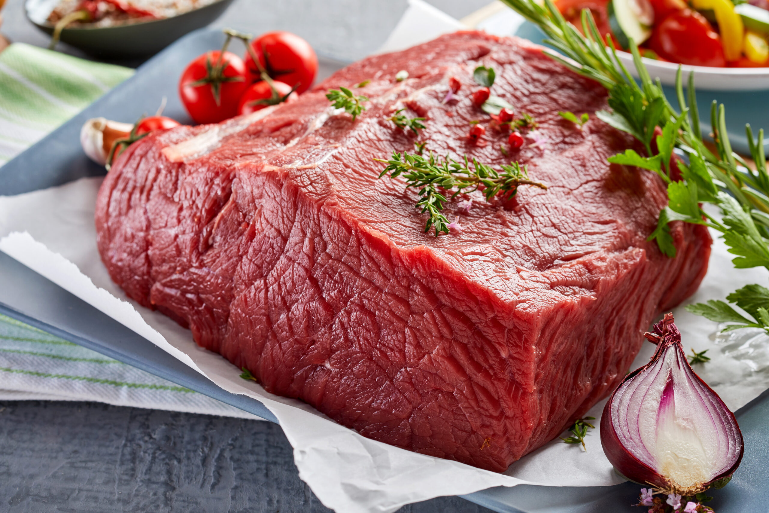 Raw beef roast garnished with herbs and vegetables, a versatile cut that could represent either chuck roast or rump roast in recipe preparation.