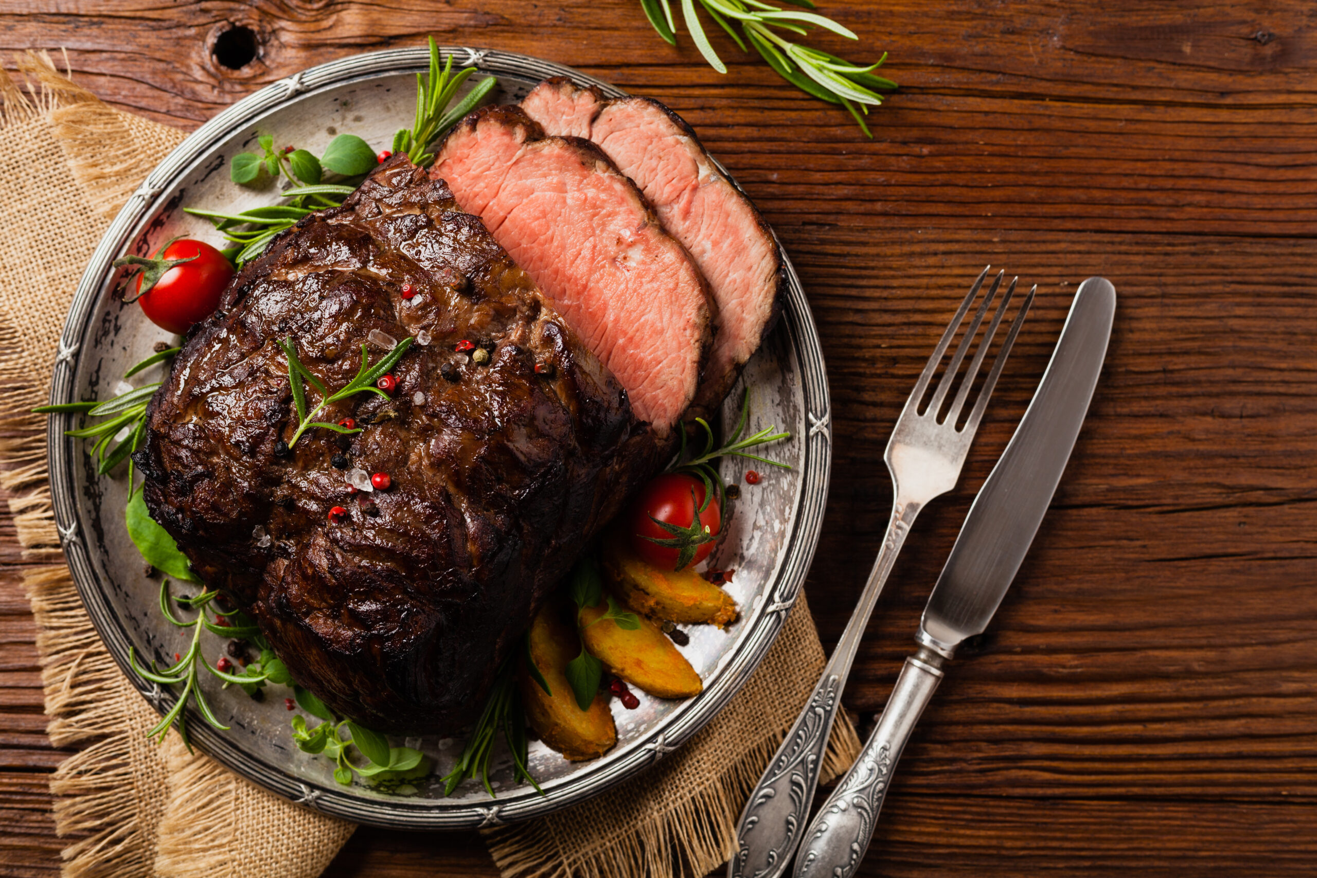 Sliced, medium-rare roast served with vegetables and herbs, visually demonstrating the final result in the chuck roast vs rump roast comparison.