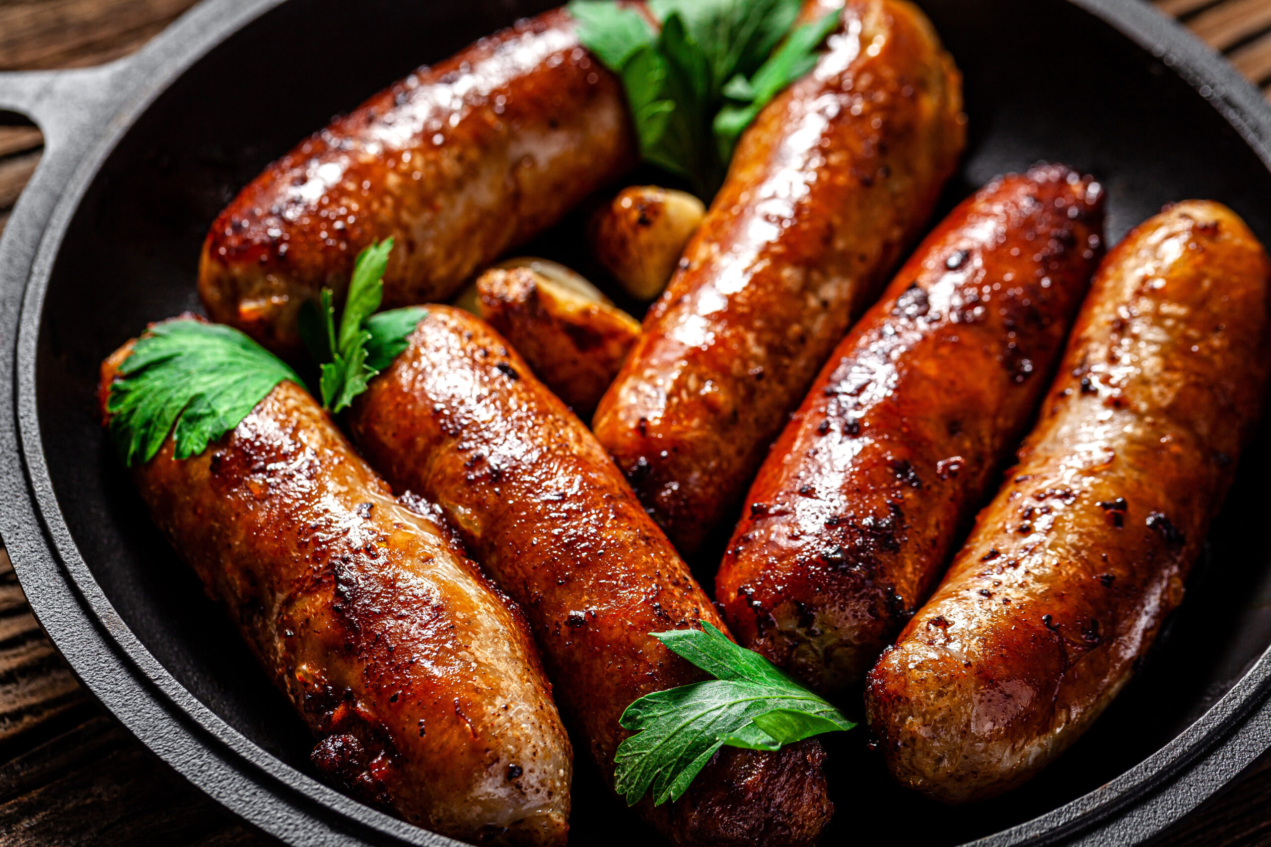 Golden brown bratwursts in a cast iron skillet with fresh herbs, highlighting alternative cooking methods beyond oven vs grill bratwurst.