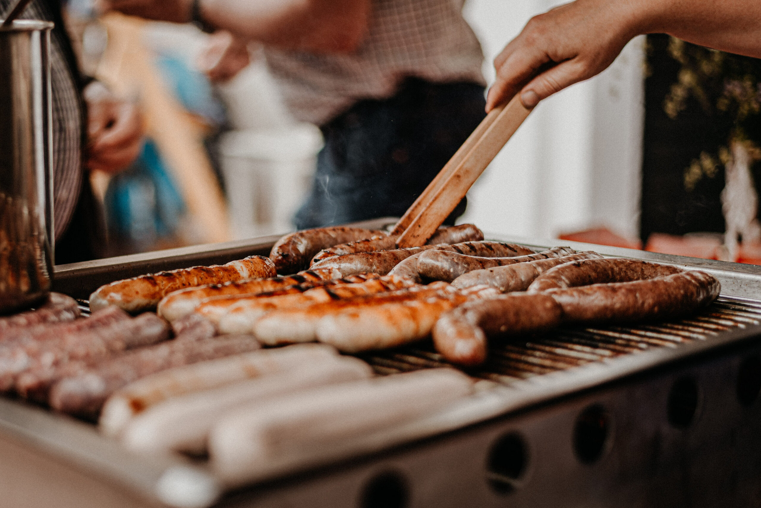 Brats being grilled and checked with tongs, demonstrating the visual cues and handling techniques for how to tell if brats are done on the grill.