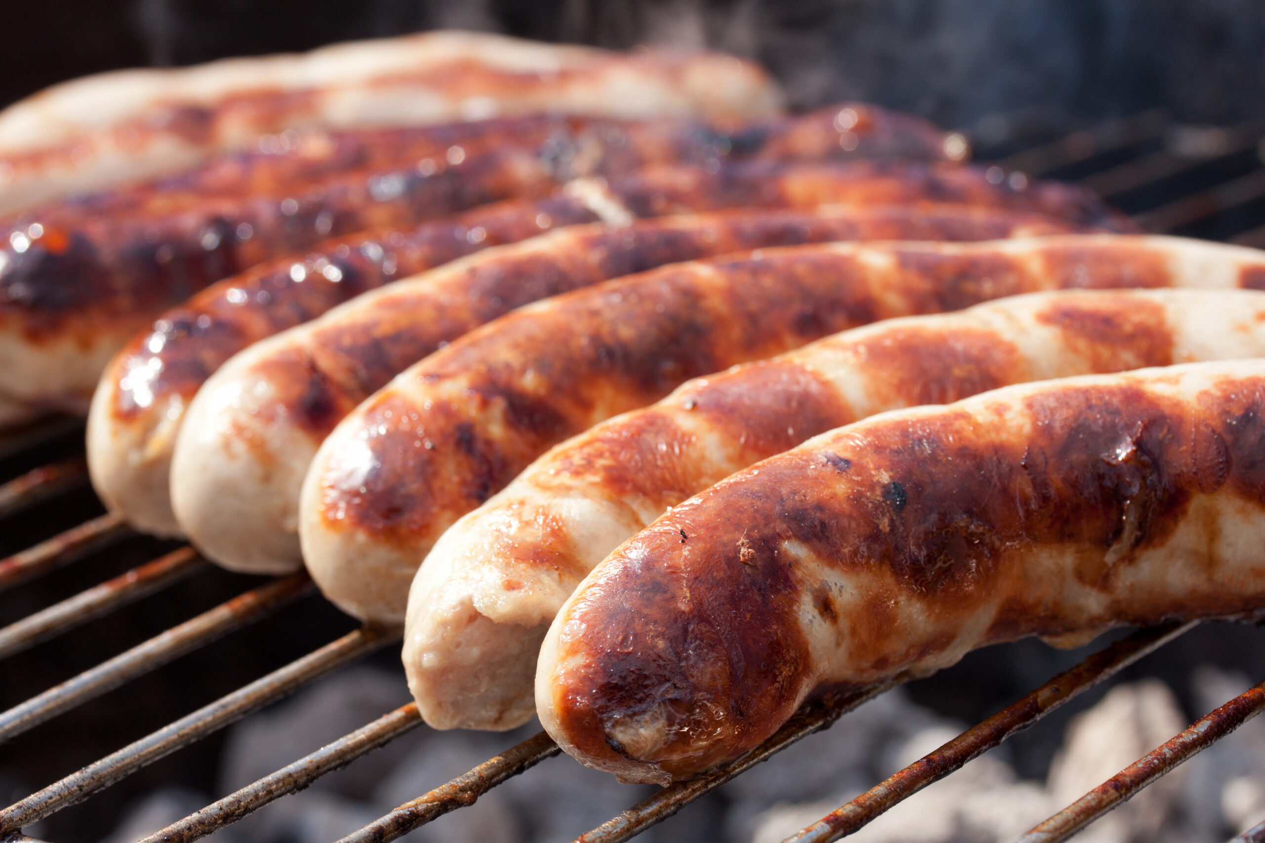Bratwursts cooking over hot coals with char marks, visually showing the flavor difference in the oven vs grill bratwurst debate.