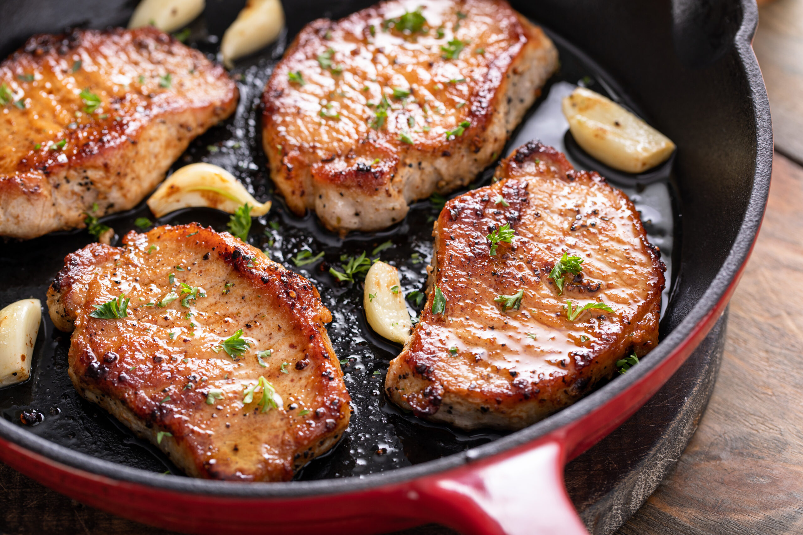 Golden brown pan fried pork cutlet seared in a skillet with garlic and herbs, showing crisp texture and juicy interior.