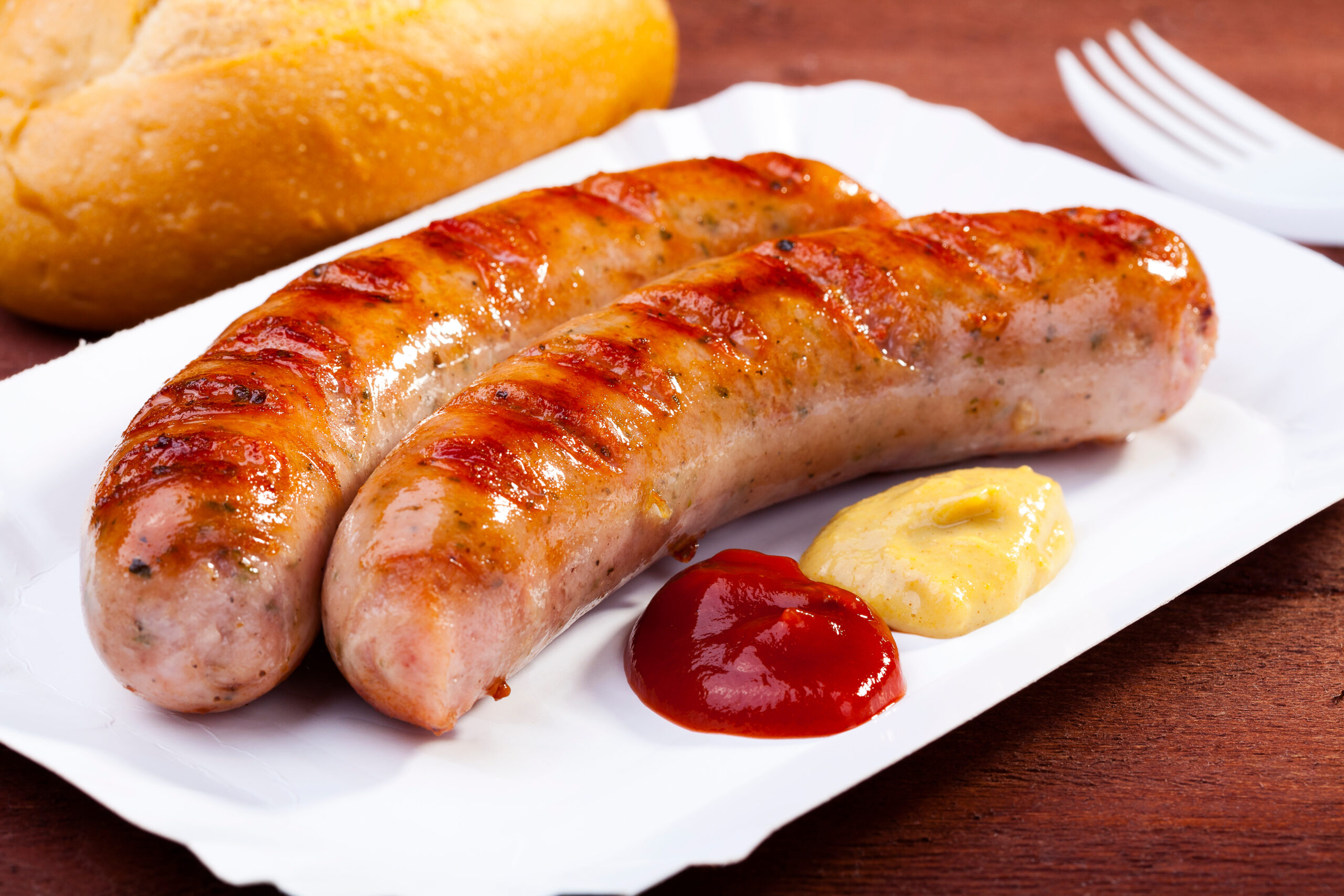 Roasted sausage with bread served on a paper tray Perfectly cooked brats served with mustard and ketchup, representing the final result after following USDA guidelines on how long to bake brats.